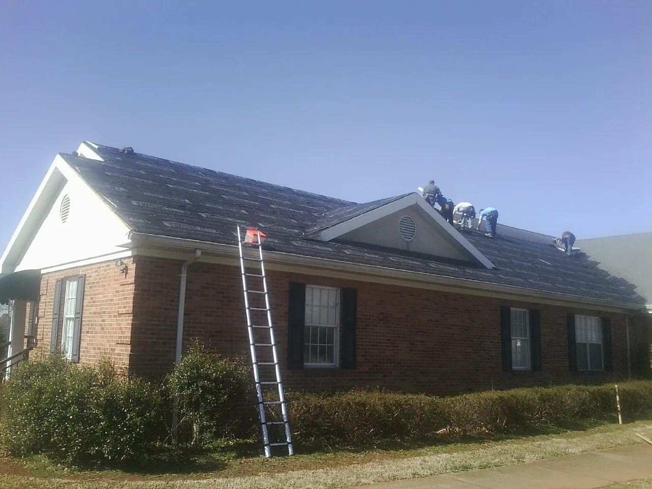 Crew tearing shingles off a brick ranch roof with a ladder set — Metal Roof Repair work by our crew in Hill City