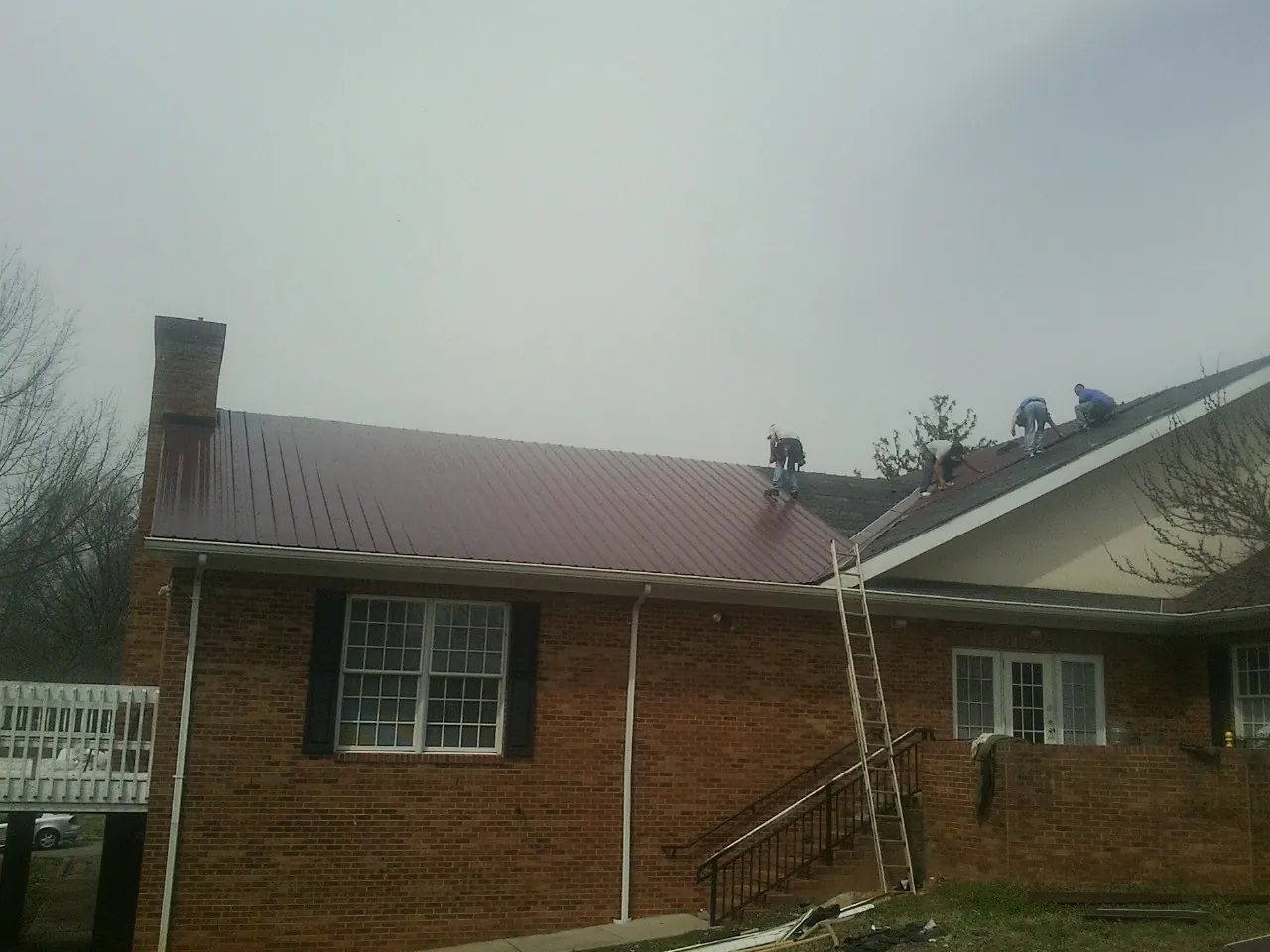 Crew setting red metal roofing panels on a brick home in Hill City