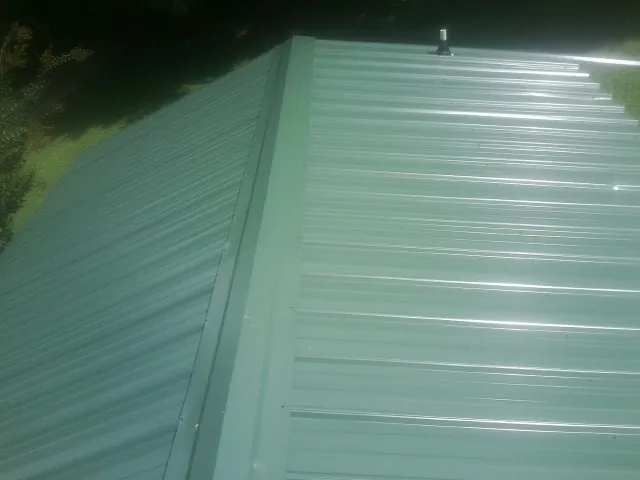 New green metal panels meeting at the ridge of a roof — Flat Roof Repair work by our crew in Hill City