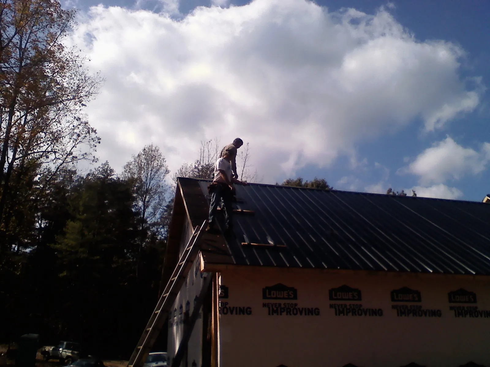 Roofer fastening dark metal panels high against a cloudy sky, from a Roof Inspection job in Hill City