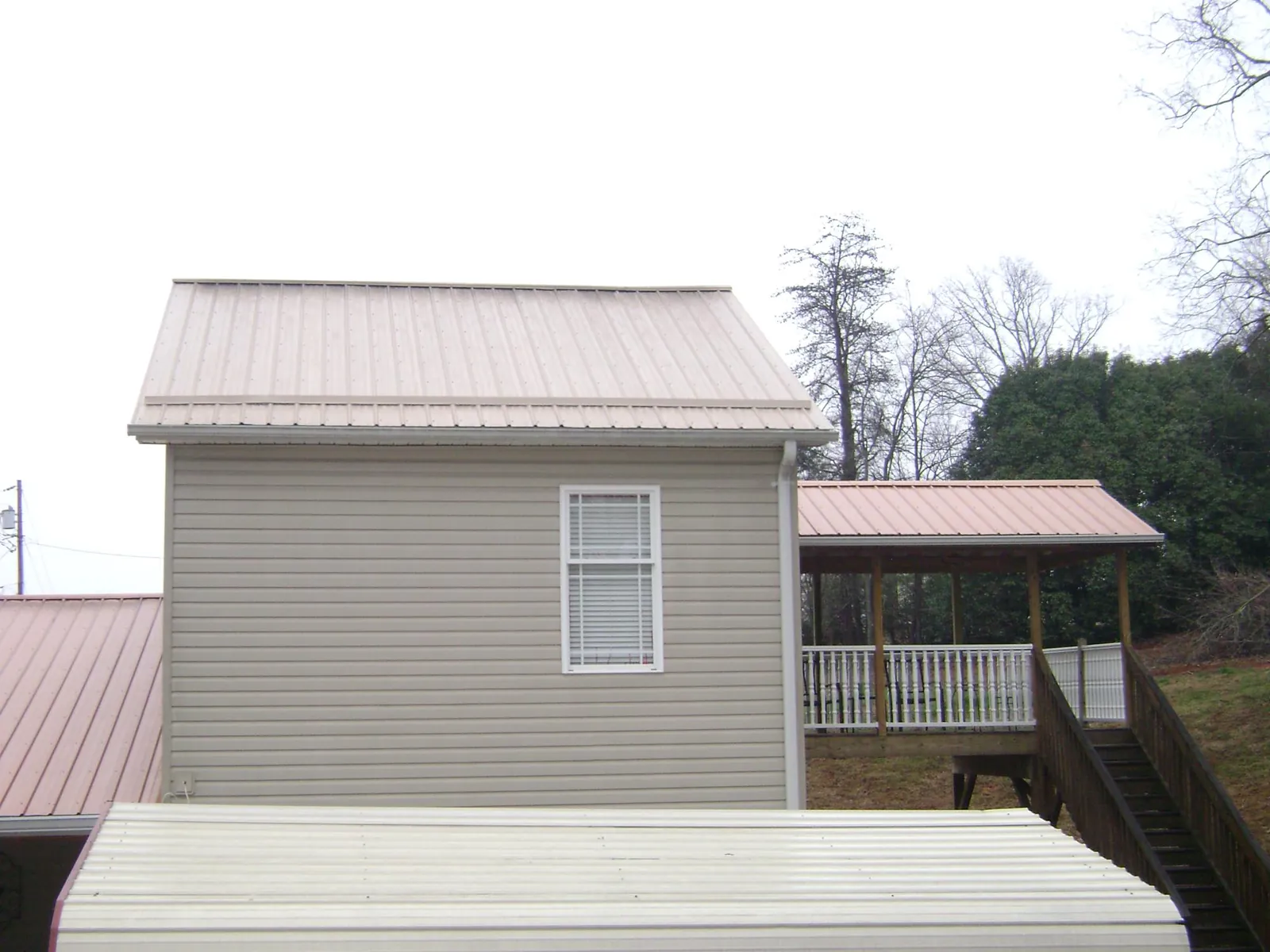 Tan metal roofs on a two story addition and attached porch, from a Roof Replacement job in Hill City